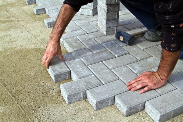 person laying gray paving stones in a herringbone pattern on a bed of sand for outdoor flooring project