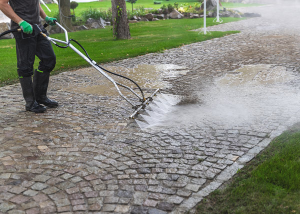person cleaning a cobblestone driveway with a high pressure water tool for effective maintenance and outdoor cleaning