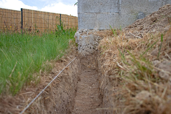 trench alongside a building foundation with grass and dirt showing clear separation for landscaping and drainage purposes