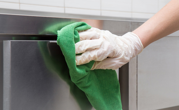 person wearing gloves cleaning stainless steel surface with green cloth professional cleaning supplies